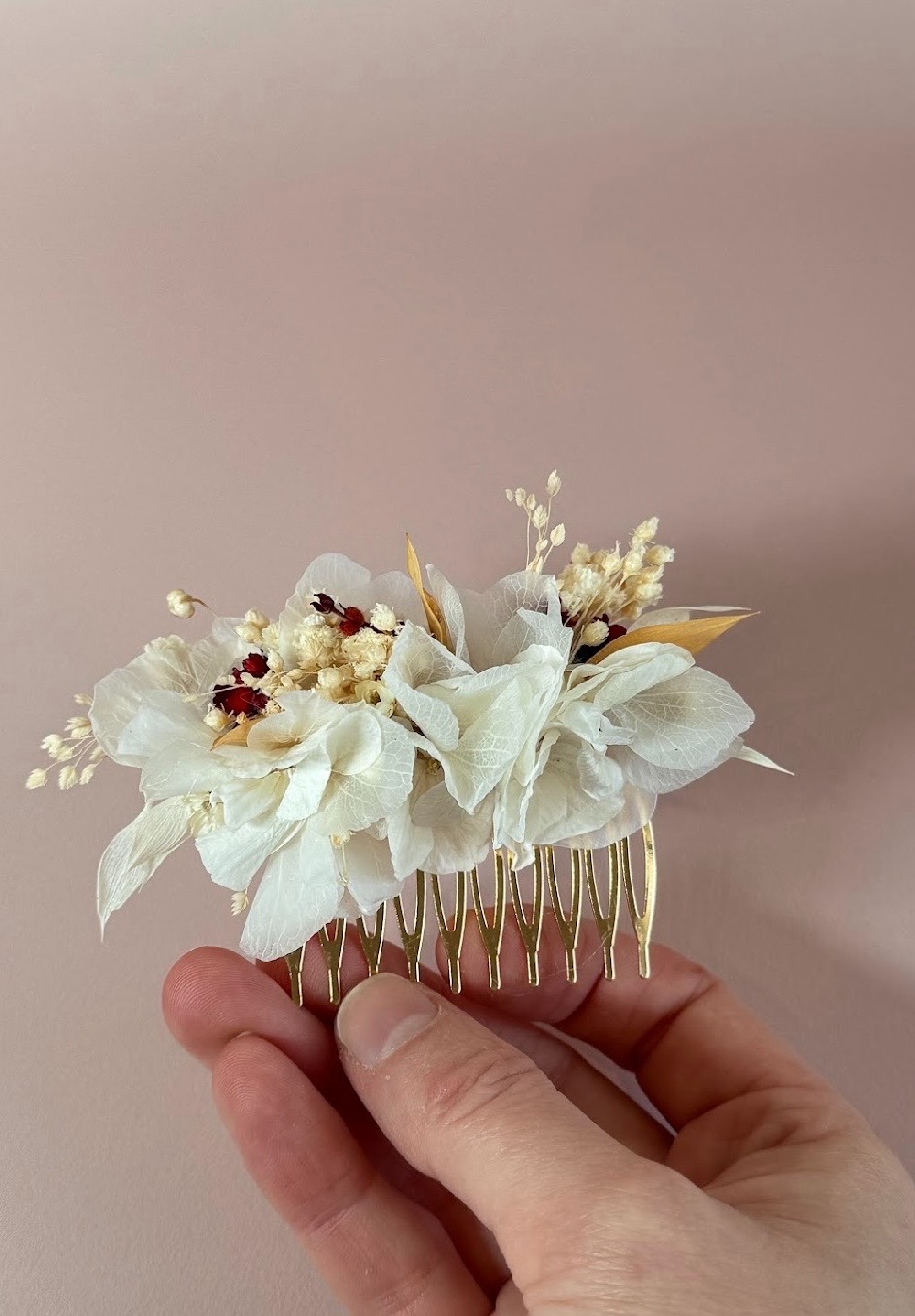 Un peigne doré garni de fleurs blanches stabilisées et de petites fleurs séchées, tenu dans une main