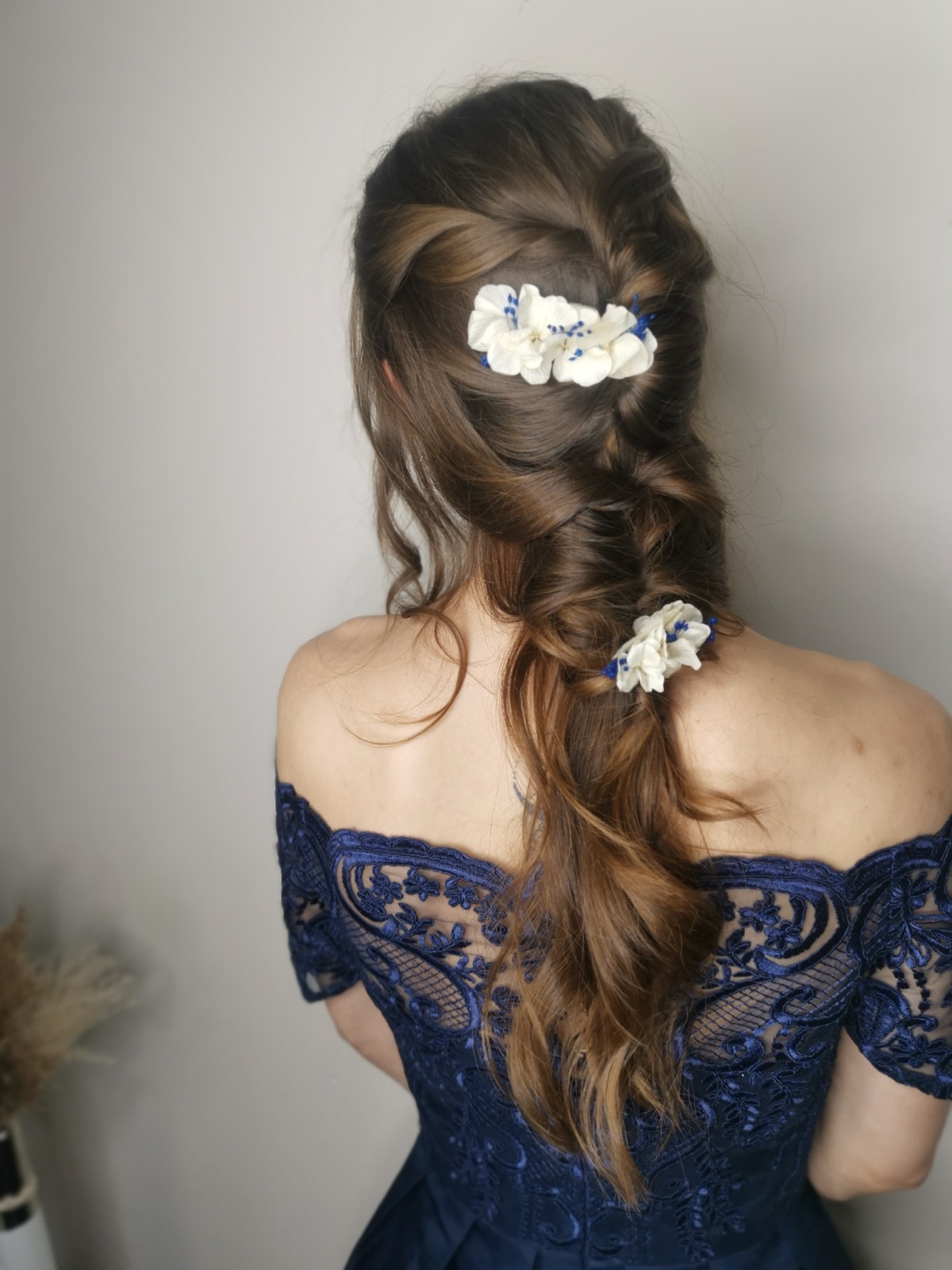 Une longue tresse bohème piquée de fleurs blanches et bleues, sur une robe bleu nuit